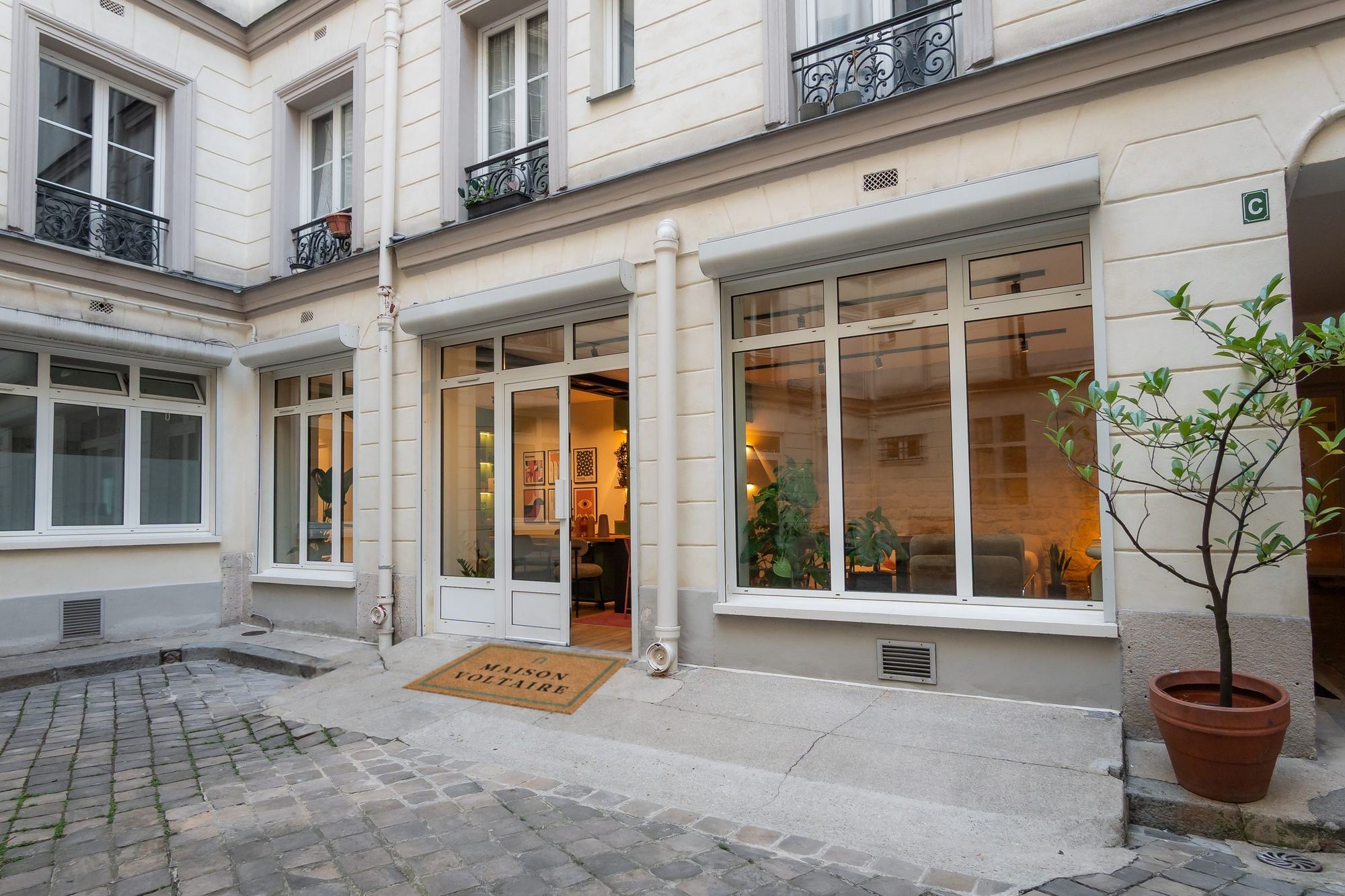 La cour pavée du 113 boulevard Voltaire, la porte ouverte sur la maison et le paillasson Maison Voltaire